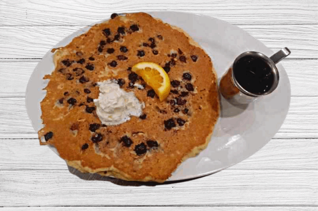 A Culinary Journey: Breakfast at Hash House A Go Go at The Plaza 1 A giant blueberry pancake from Hash House A Go Go, topped with whipped butter, an orange slice, and syrup—perfect for starting your breakfast journey.