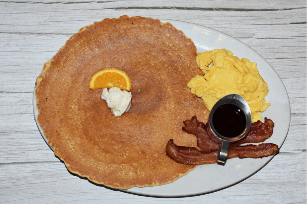 The Plaza’s Breakfast Scene Just Got Better with Hash House A Go Go 1 Hash House A Go Go’s oversized pancake breakfast with eggs, bacon, syrup, and a fresh orange garnish—perfect for brunch with a view in Las Vegas.