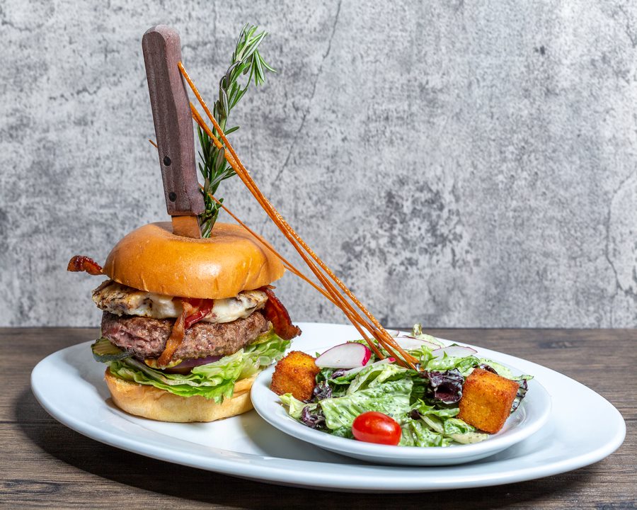 A towering burger with bacon, lettuce, and cheese served with a side salad—perfect for your first visit to Hash House A Go Go.

