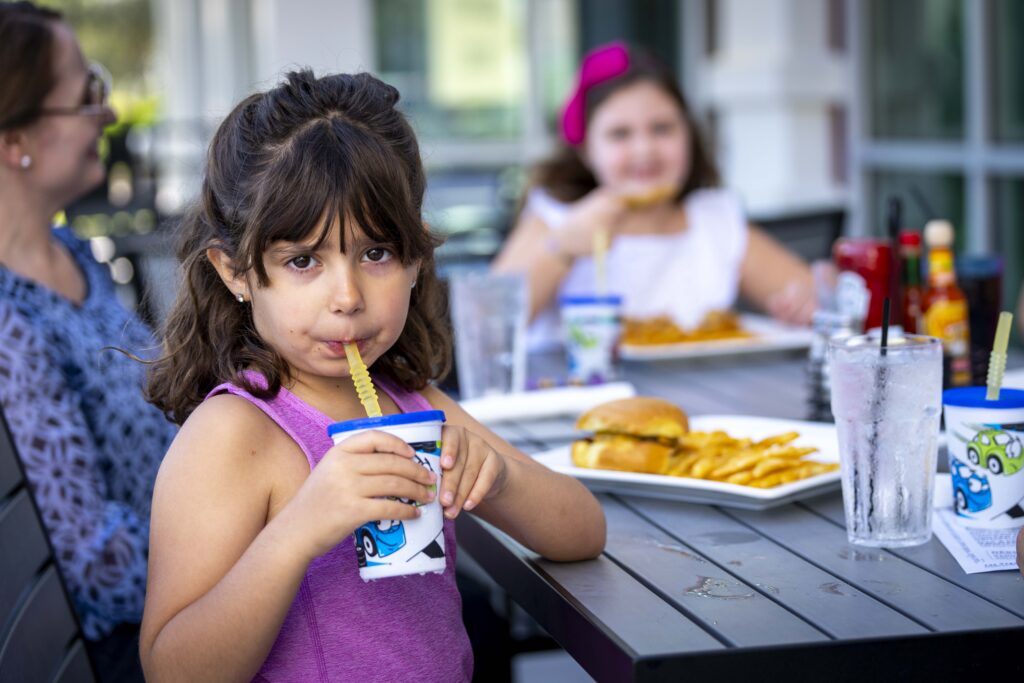 Family Dining Perfected at Hash House A Go Go The Plaza 1 Young girl sipping a drink at a family-friendly outdoor dining table at Hash House A Go Go